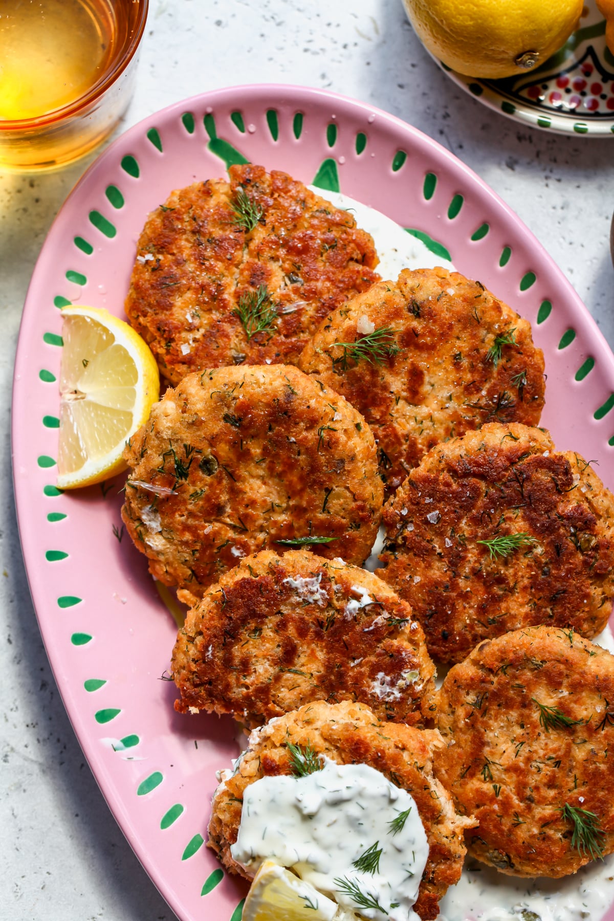 Salmon patties arranged on an oval pink platter with lemon wedges scattered around them.