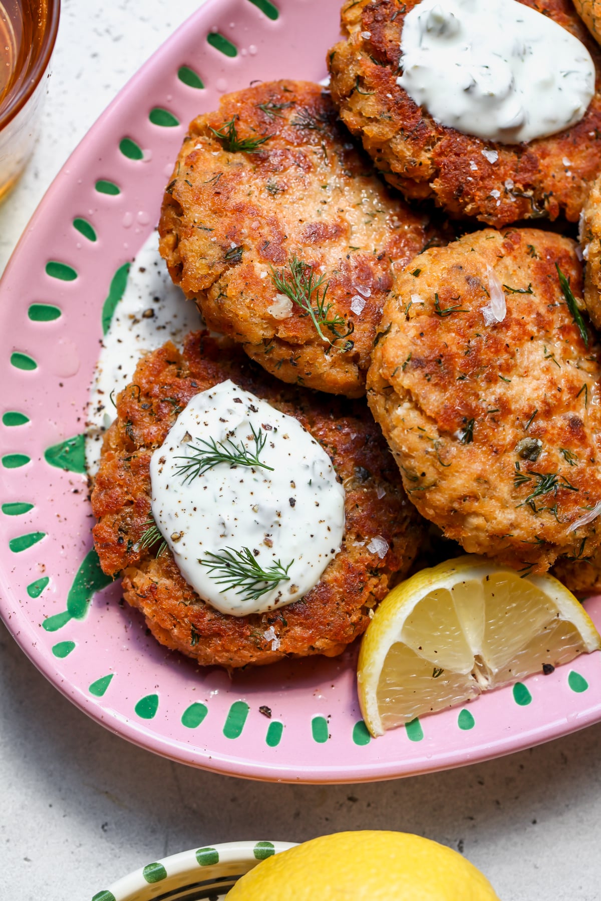 Salmon patties arranged on a pink platter topped with a dollop of tartar sauce and fresh dill.