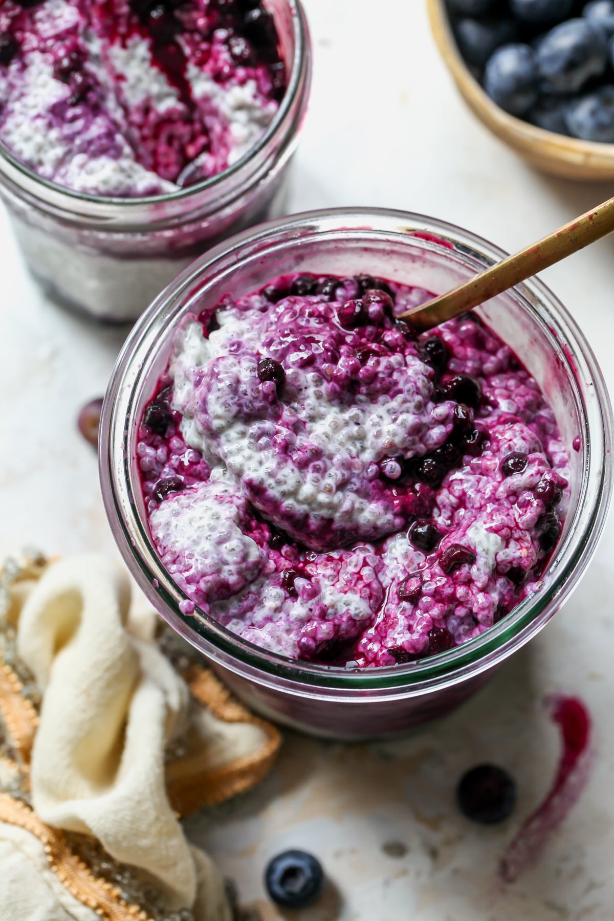 A spoon digging into a glass jar of Earl Grey Chia Pudding layered with Wild Blueberry Compote.