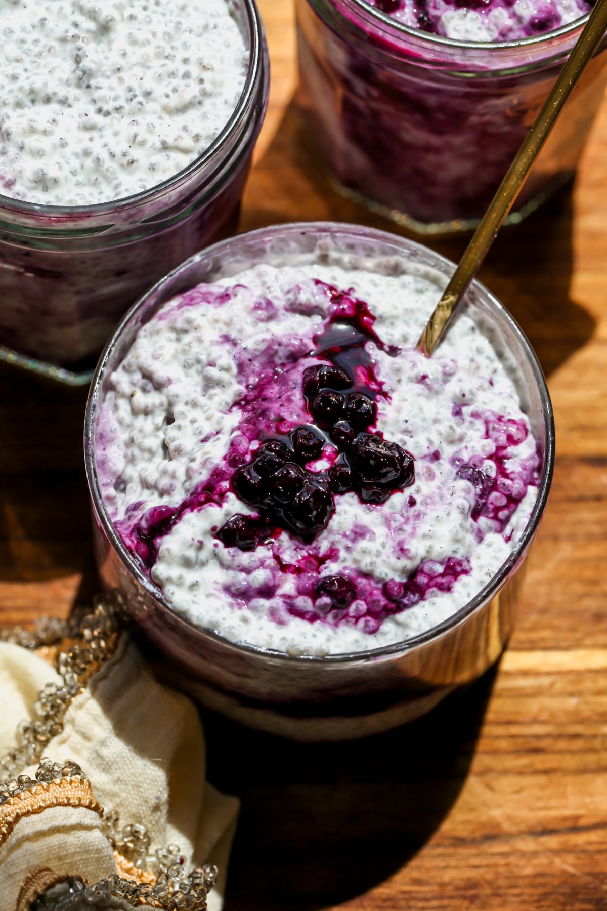 Earl Grey Chia Pudding with Wild Blueberry Compote styled in a clear glass jar on a wooden cutting board.