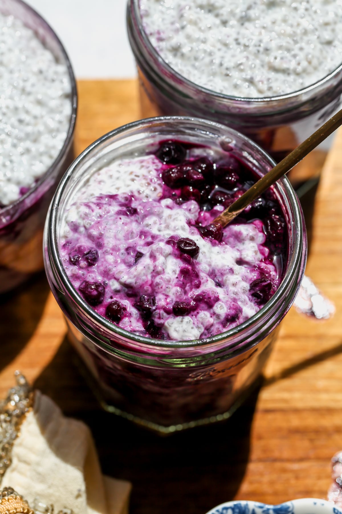 A gold spoon digging into a jar of Earl Grey Chia Pudding with Wild Blueberry Compote.