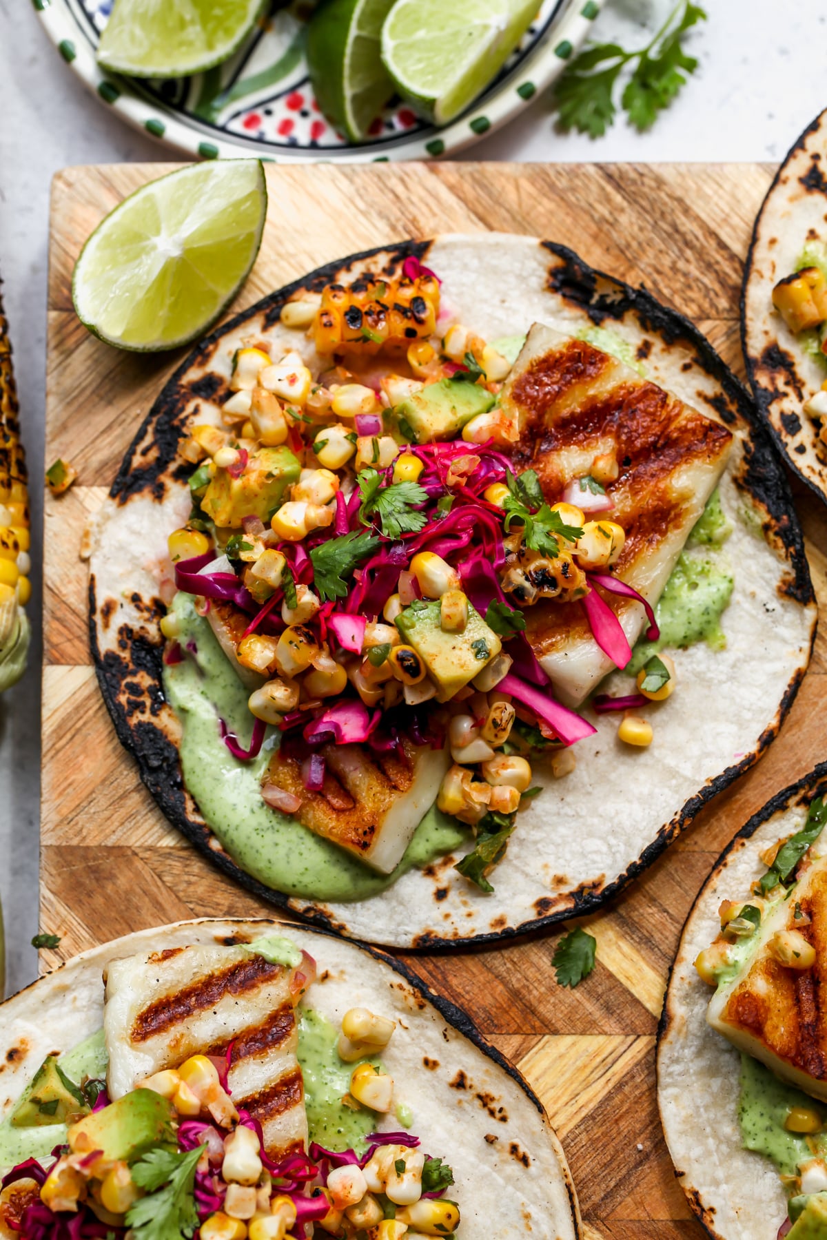 Charred corn tortillas topped with grilled halloumi cheese, corn salad, pickled cabbage, and creamy green sauce.