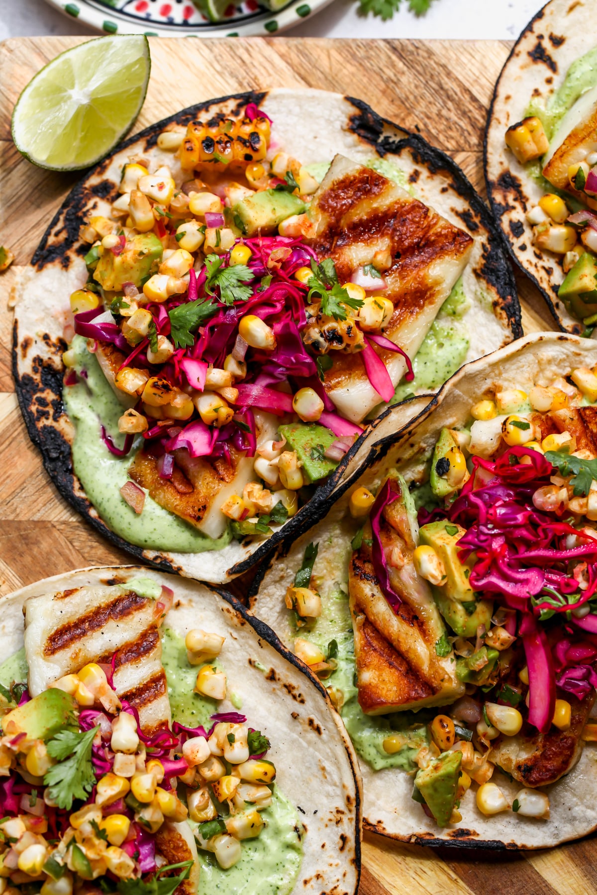 Grilled Halloumi Tacos topped with corn salad and red cabbage arranged on a wooden board.