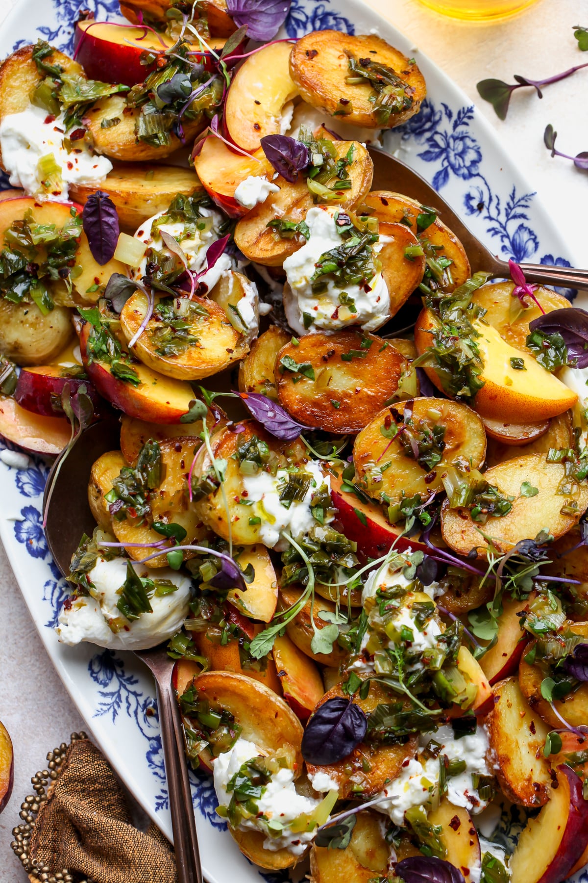 Crispy Potato Salad with Peaches and Charred Scallion Dressing styled on a white and blue floral platter.
