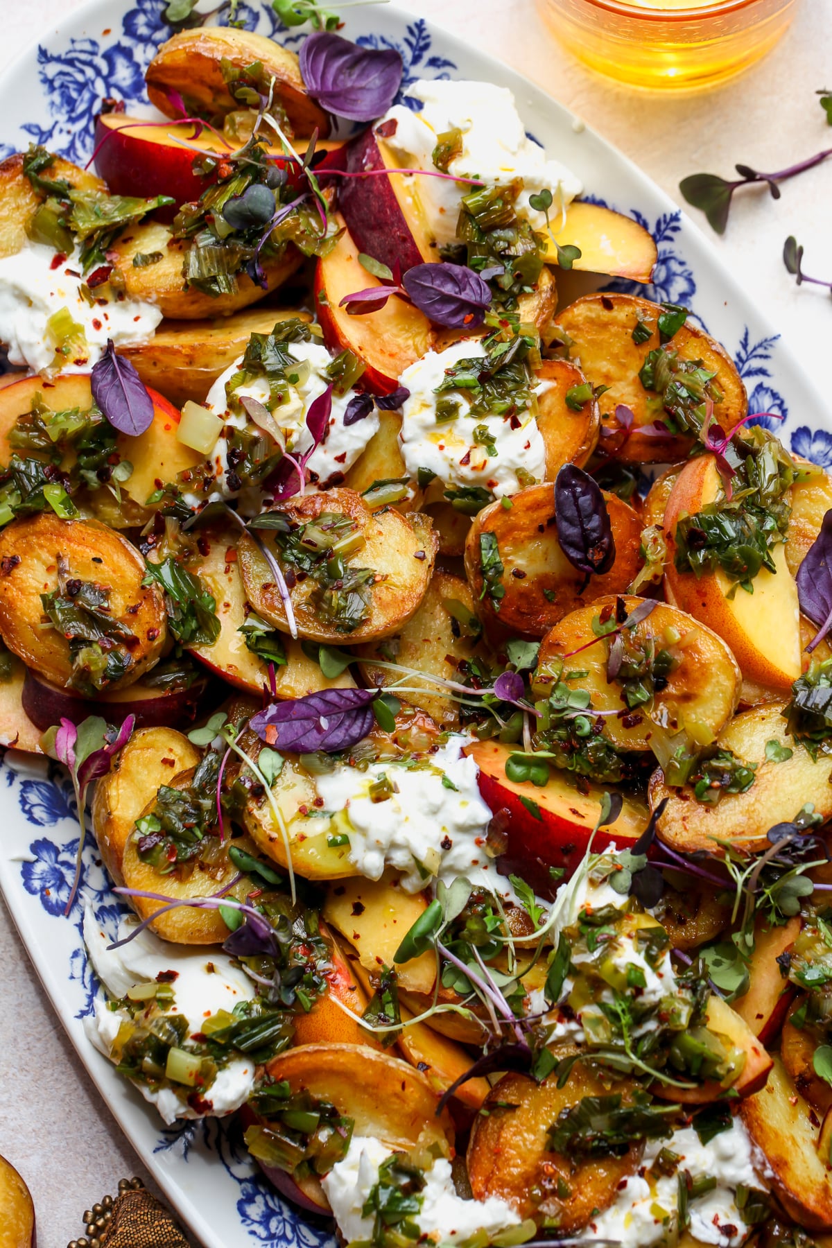 Crispy potato salad with sliced peaches, burrata, and scallion dressing assembled on a serving platter.
