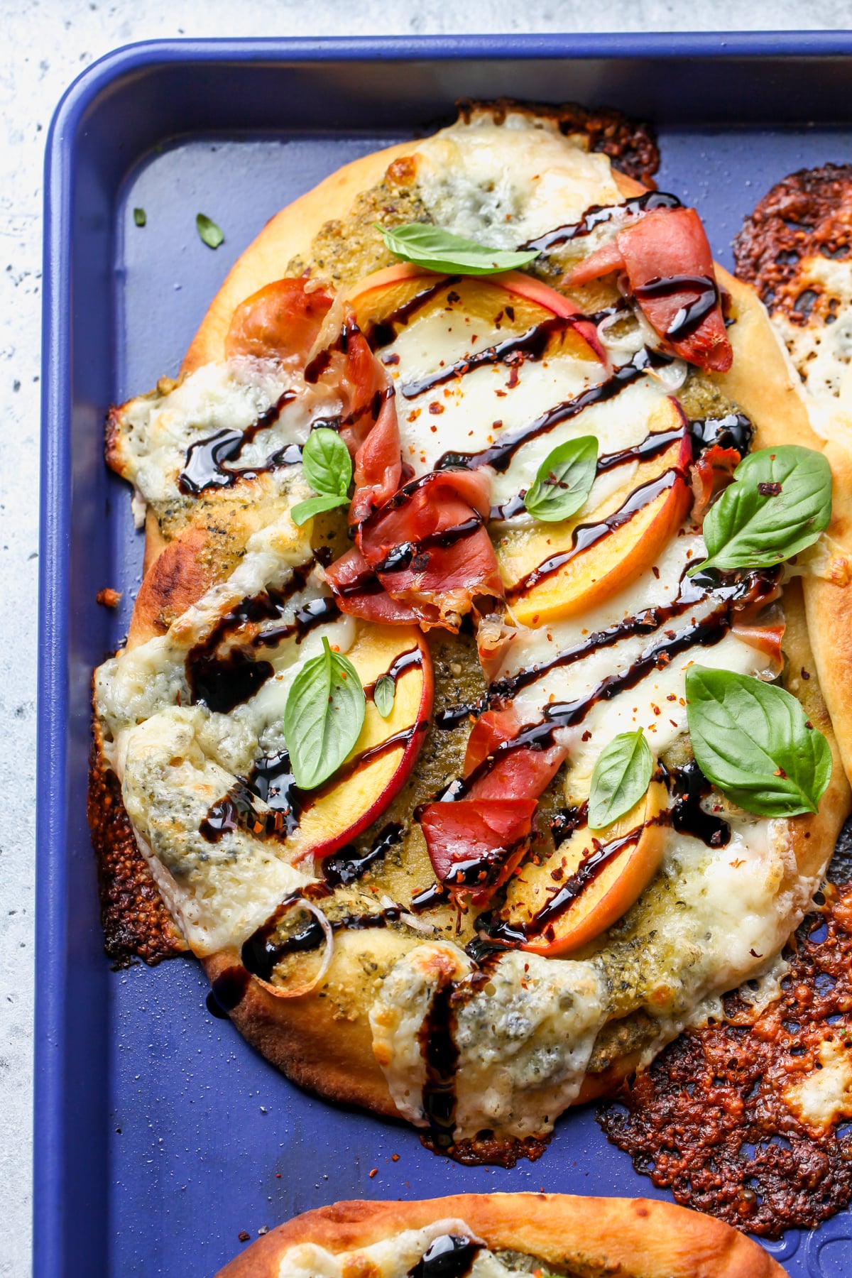 Summer Naan Pizza on a blue baking sheet drizzled with balsamic and topped with fresh basil.