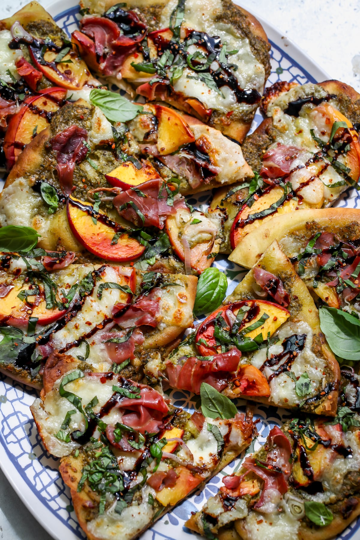 Sliced peach and prosciutto pizza arranged on a blue and white floral platter.