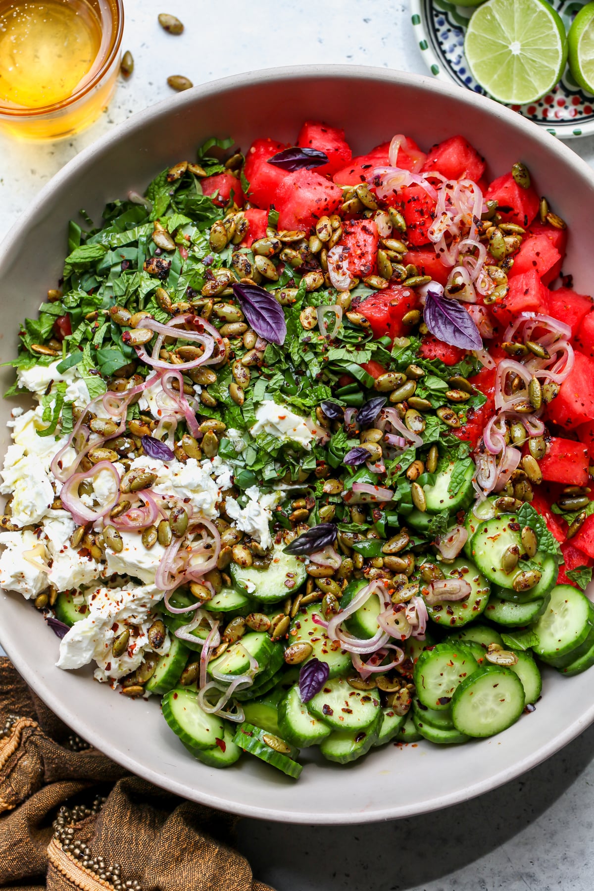 Watermelon-Cucumber Salad topped with Tajín pepitas and feta styled in a large tan bowl.