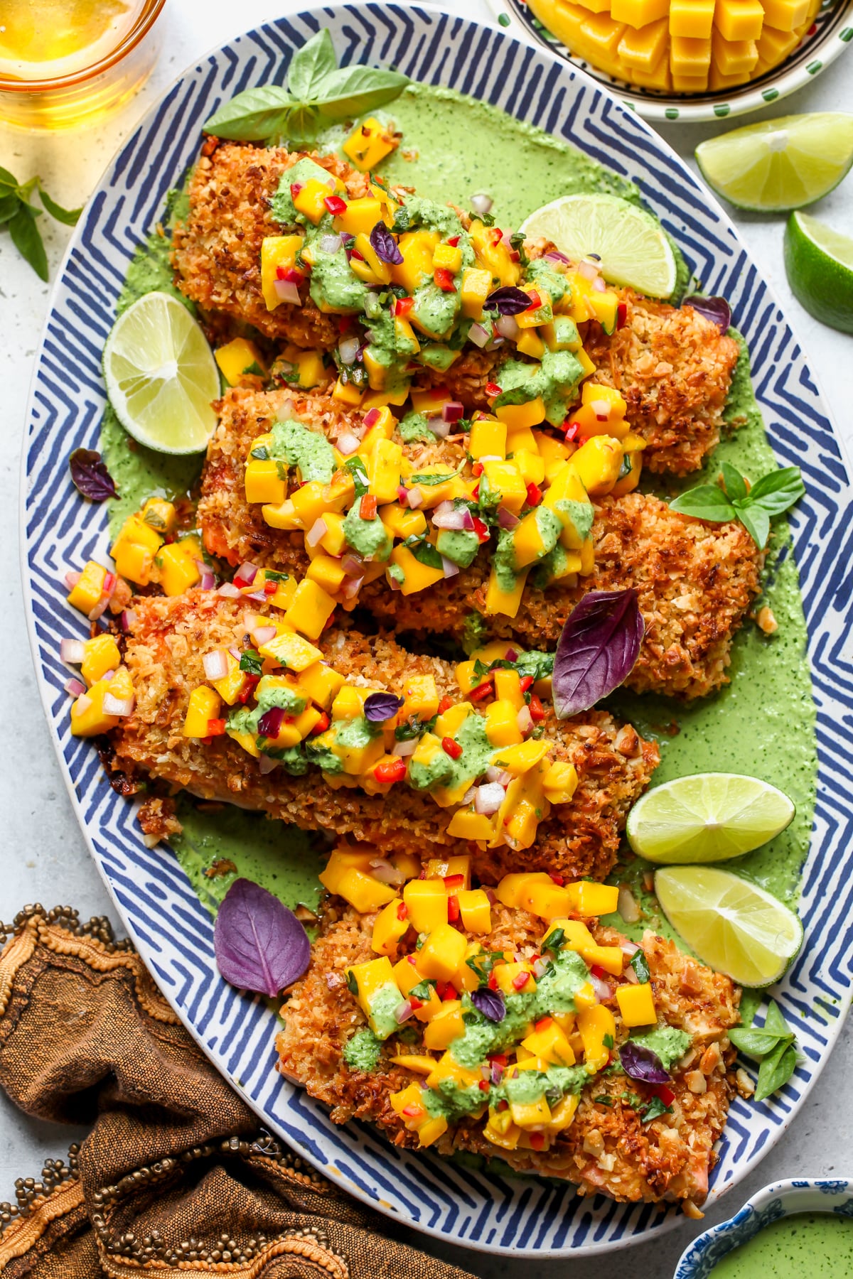 Coconut-Macadamia Crusted Salmon served over creamy basil sauce and topped with mango salsa on a blue and white platter.
