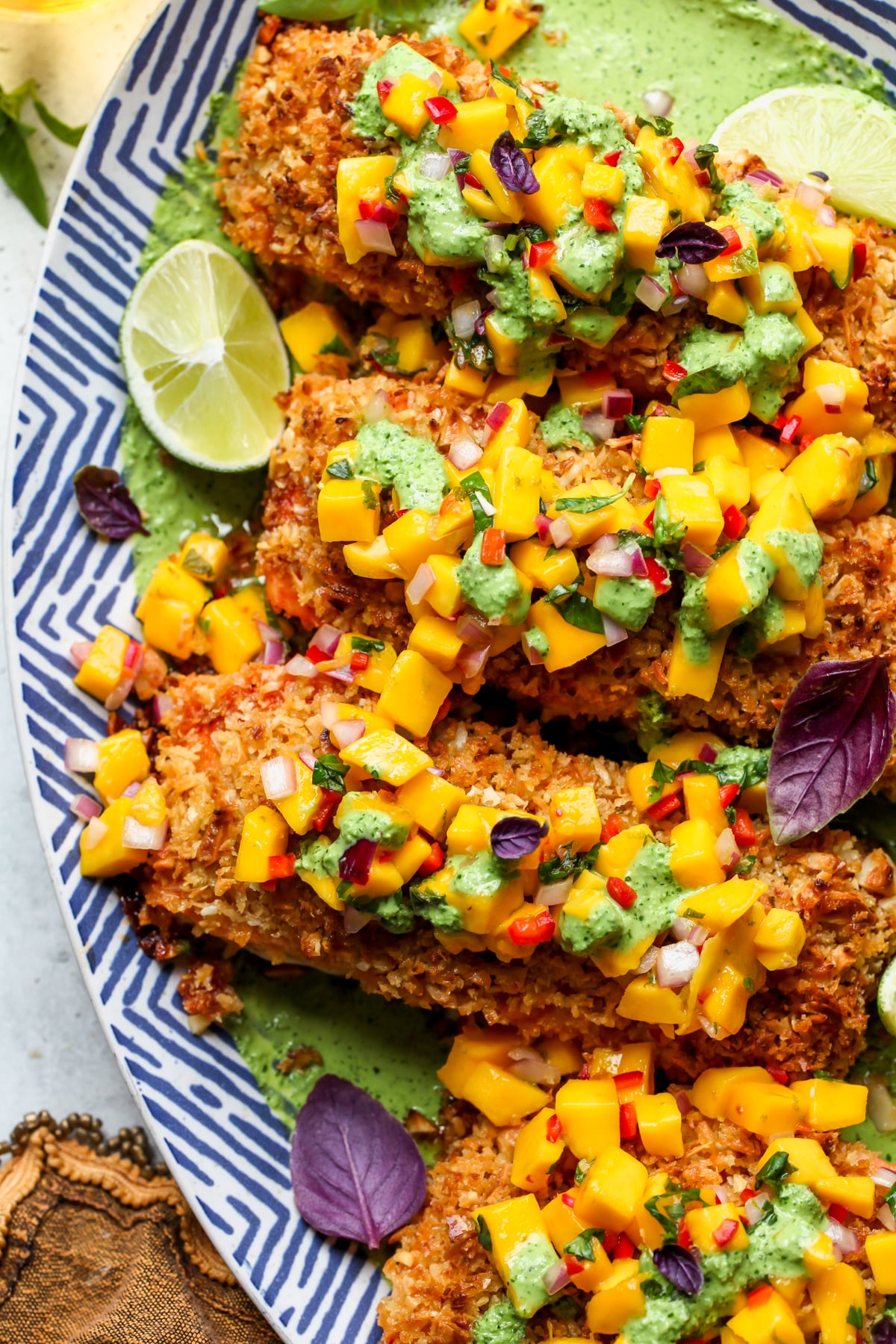 Coconut-Macadamia Crusted Salmon topped with mango salsa and creamy basil sauce styled on a blue and white serving platter.