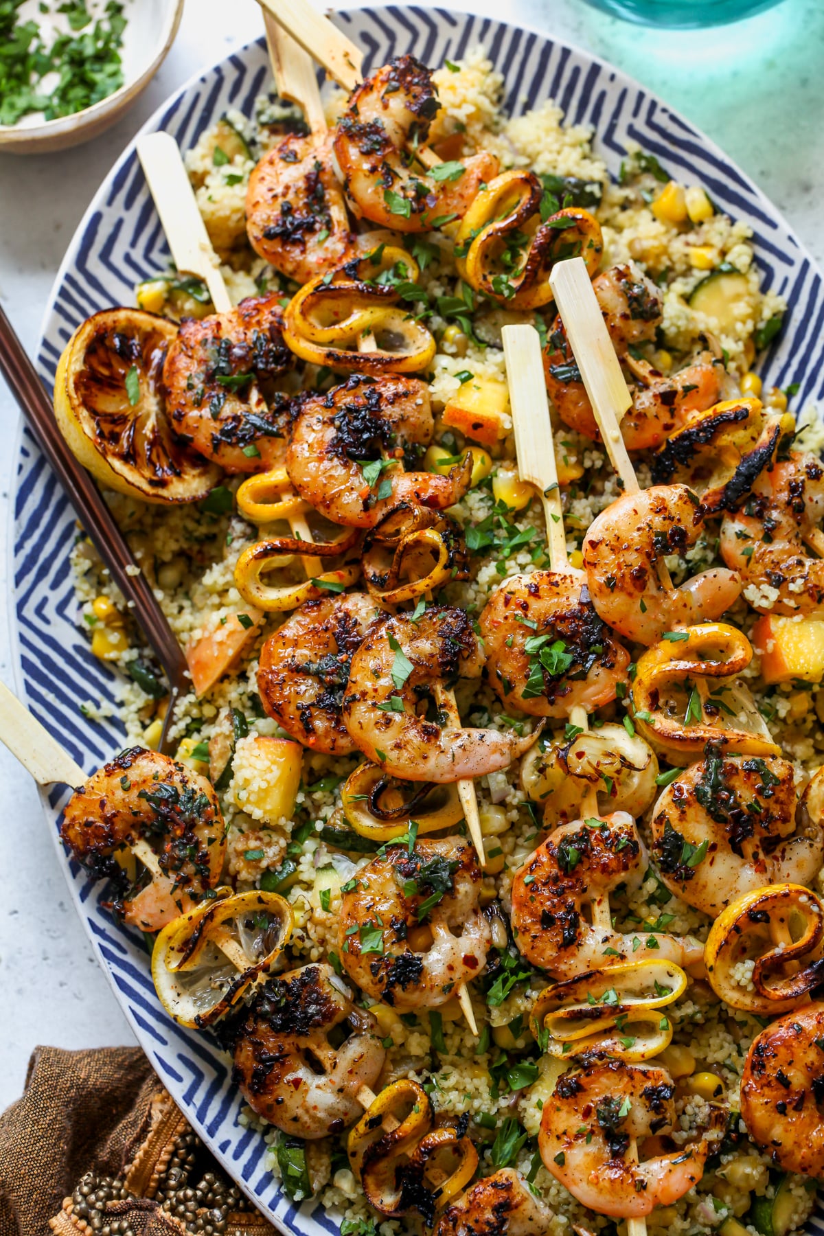Lemon Tarragon Butter Grilled Shrimp Skewers assembled over couscous salad on a white and blue serving platter.