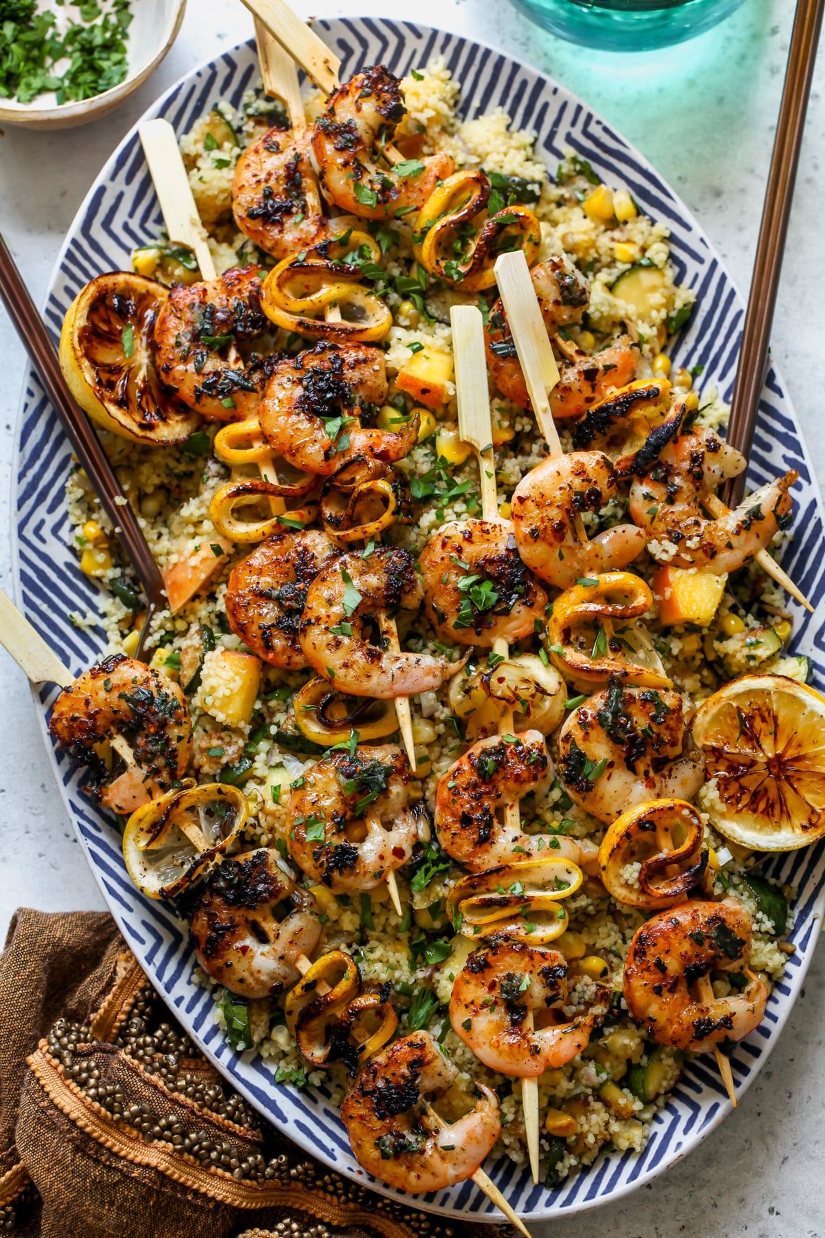 Lemon Tarragon Butter Grilled Shrimp Skewers served over summer couscous salad on a white and blue serving platter.
