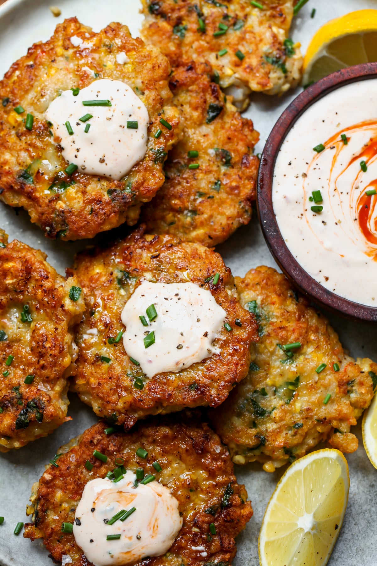 Shrimp cakes arranged on a plate topped with dollops of creamy sriracha sauce.