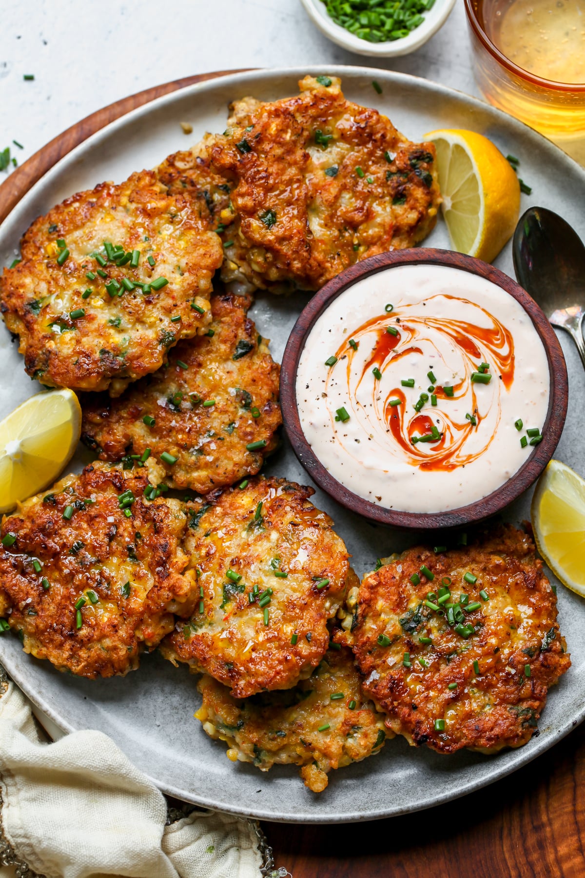 Old Bay Shrimp and Corn Cakes arranged on a plate with a bowl of sriracha sauce on the right side.
