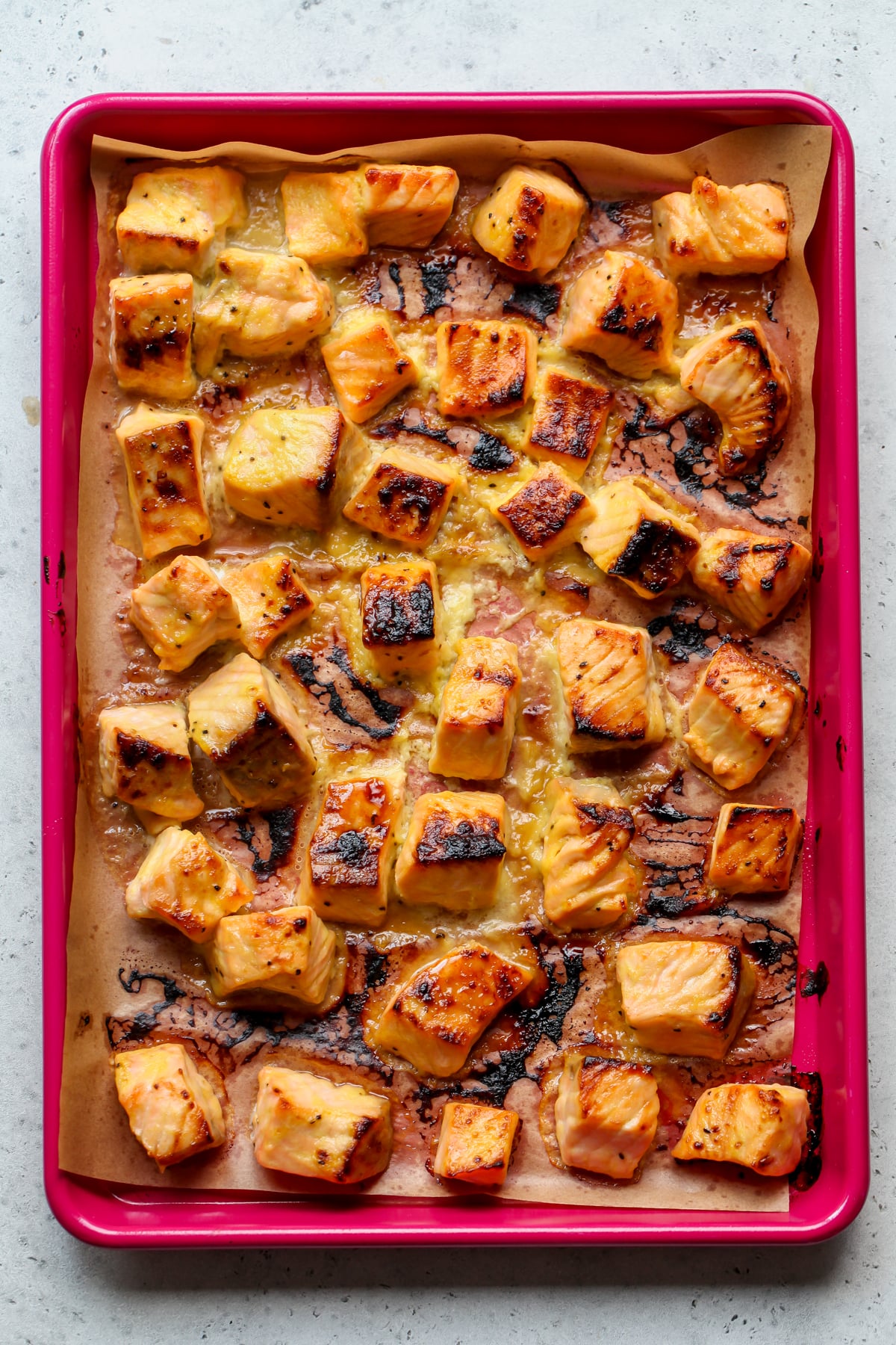 Cubes of broiled, caramelized salmon on a parchment-lined pink baking sheet.