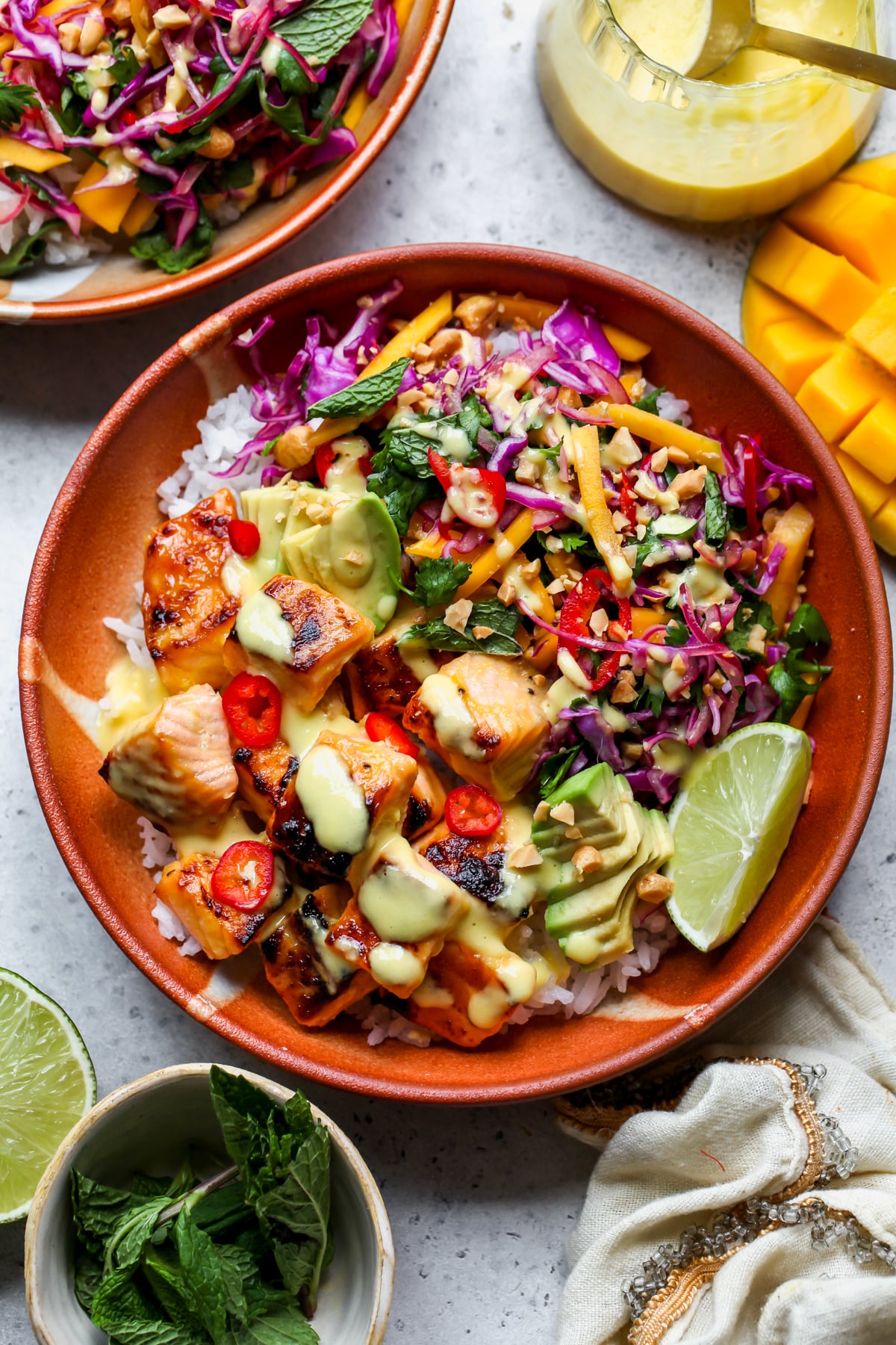 Mango-Miso Glazed Salmon Bowls styled in orange bowls on a gray surface.
