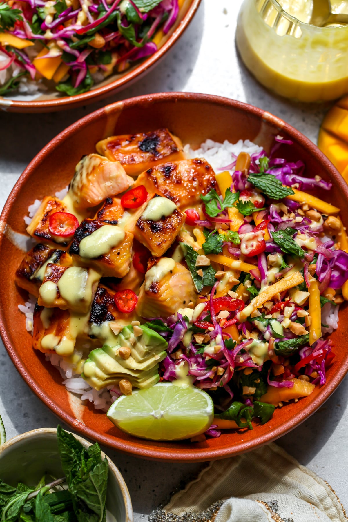 Mango-Miso Glazed Salmon Bowls styled in an orange bowl with thai slaw and sliced avocado.