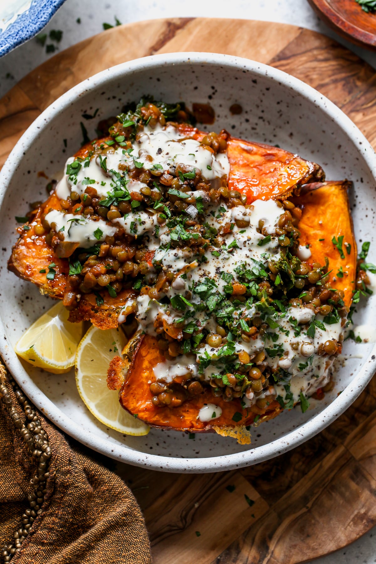 Harissa lentil sweet potatoes styled in a white bowl topped with lemon tahini sauce and fresh parsley.