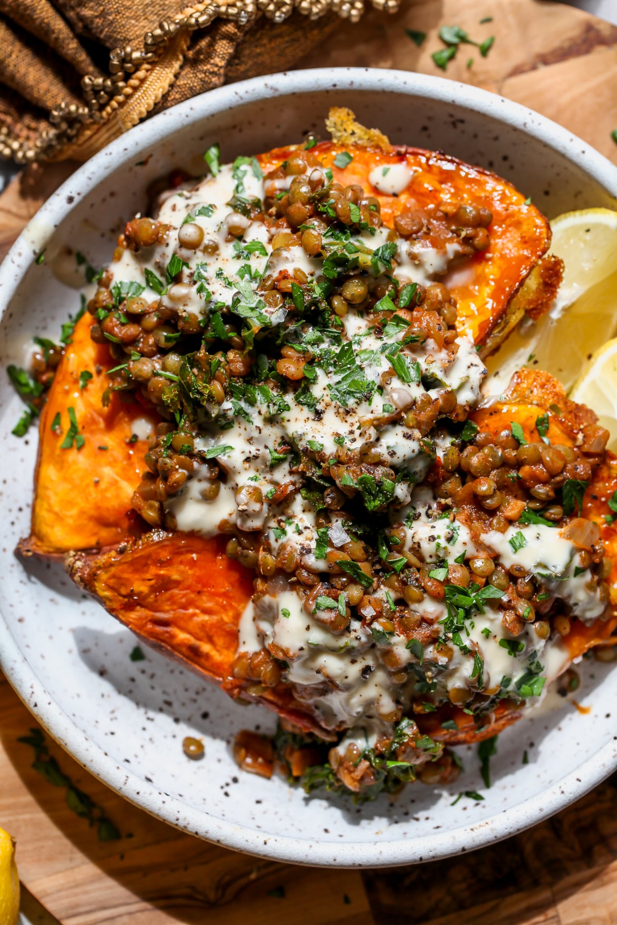 Harissa lentil sweet potatoes styled in a white bowl topped with lemon tahini sauce and fresh herbs.
