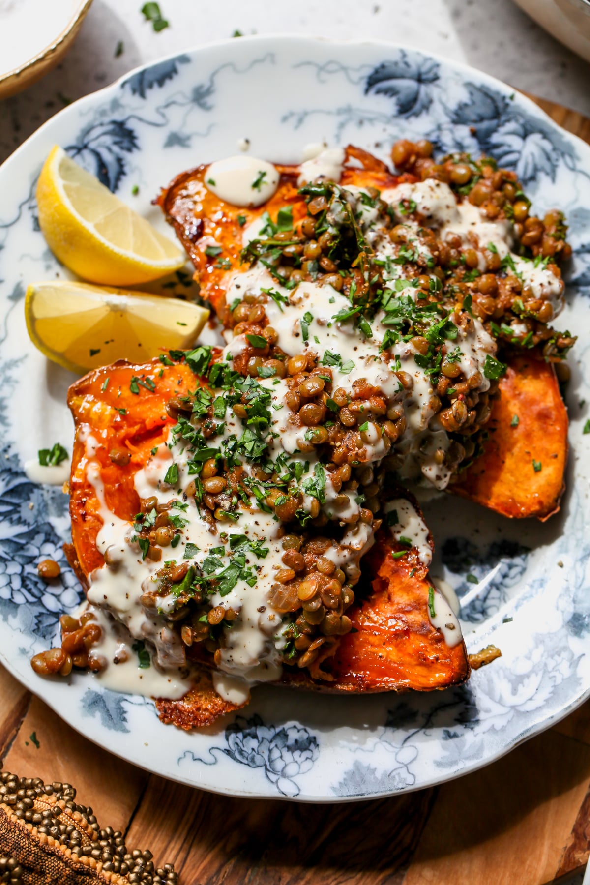 Two sweet potato halves topped with harissa lentils, lemony tahini sauce, and chopped fresh parsley.