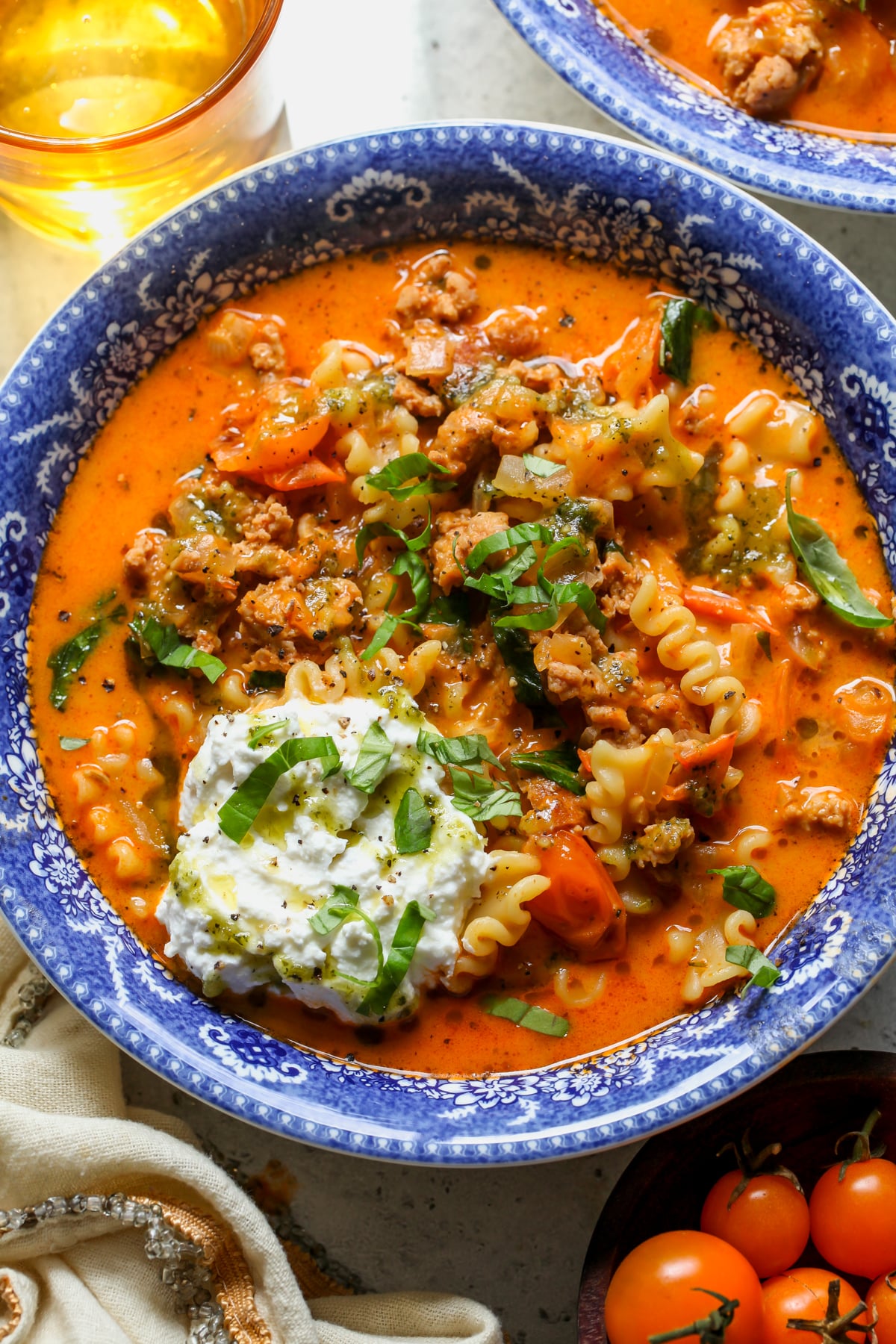 Sungold Tomato Lasagna Soup styled in a blue and white bowl topped with ricotta and pesto oil.
