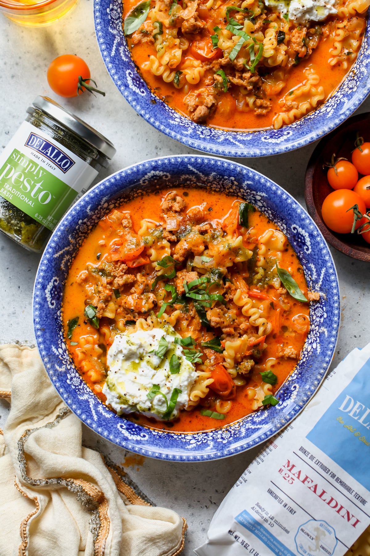Two bowls of lasagna soup styled on a gray surface next to DeLallo pasta products.