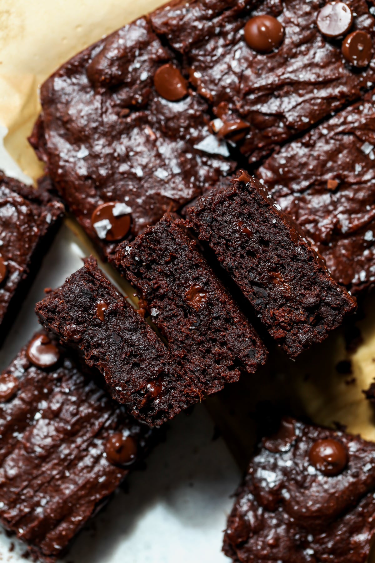 Squares of sweet potato brownies arranged on a piece of parchment paper on a white surface.