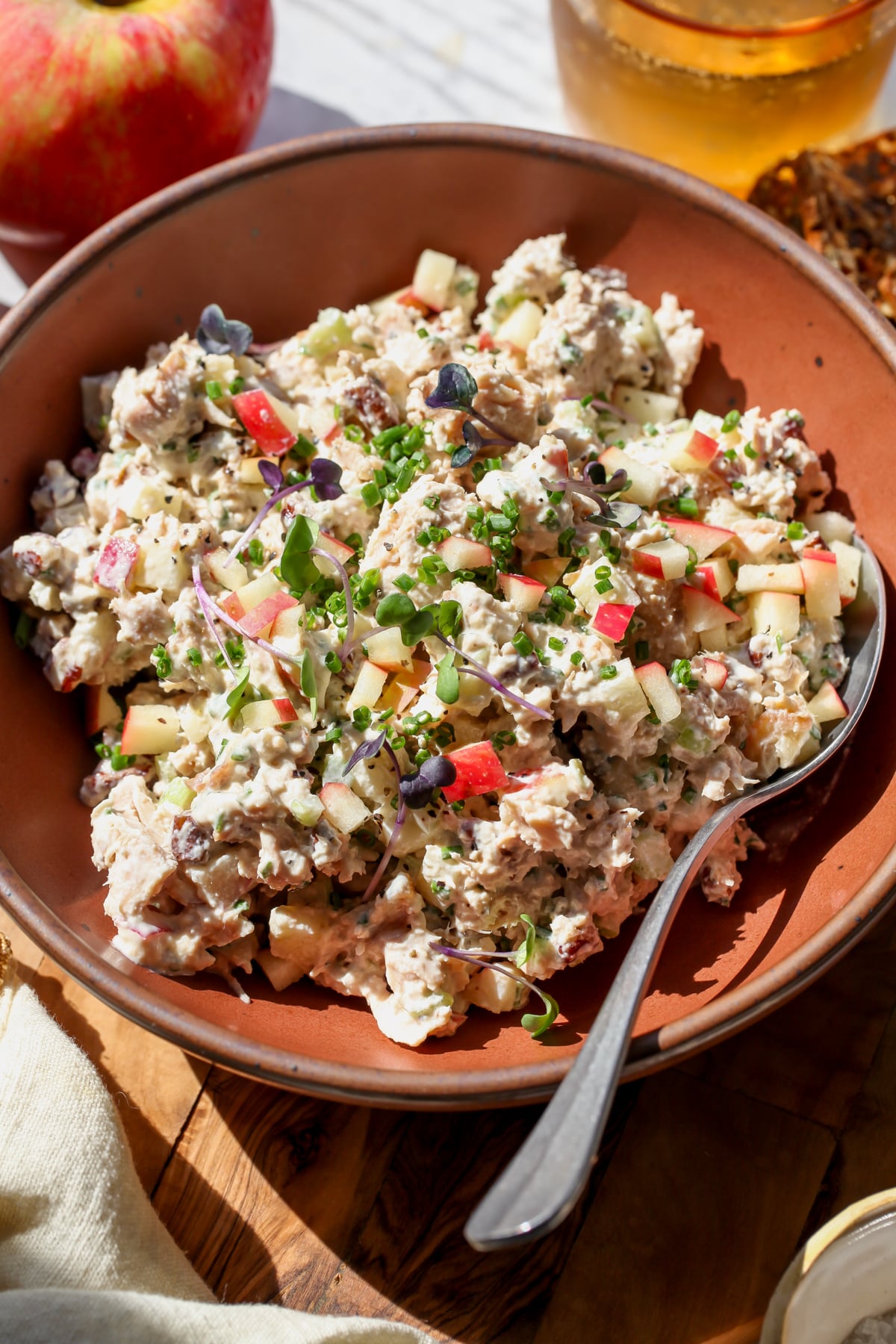 Apple-Chive Tuna Salad styled in a maroon serving bowl with a spoon resting on the right side.