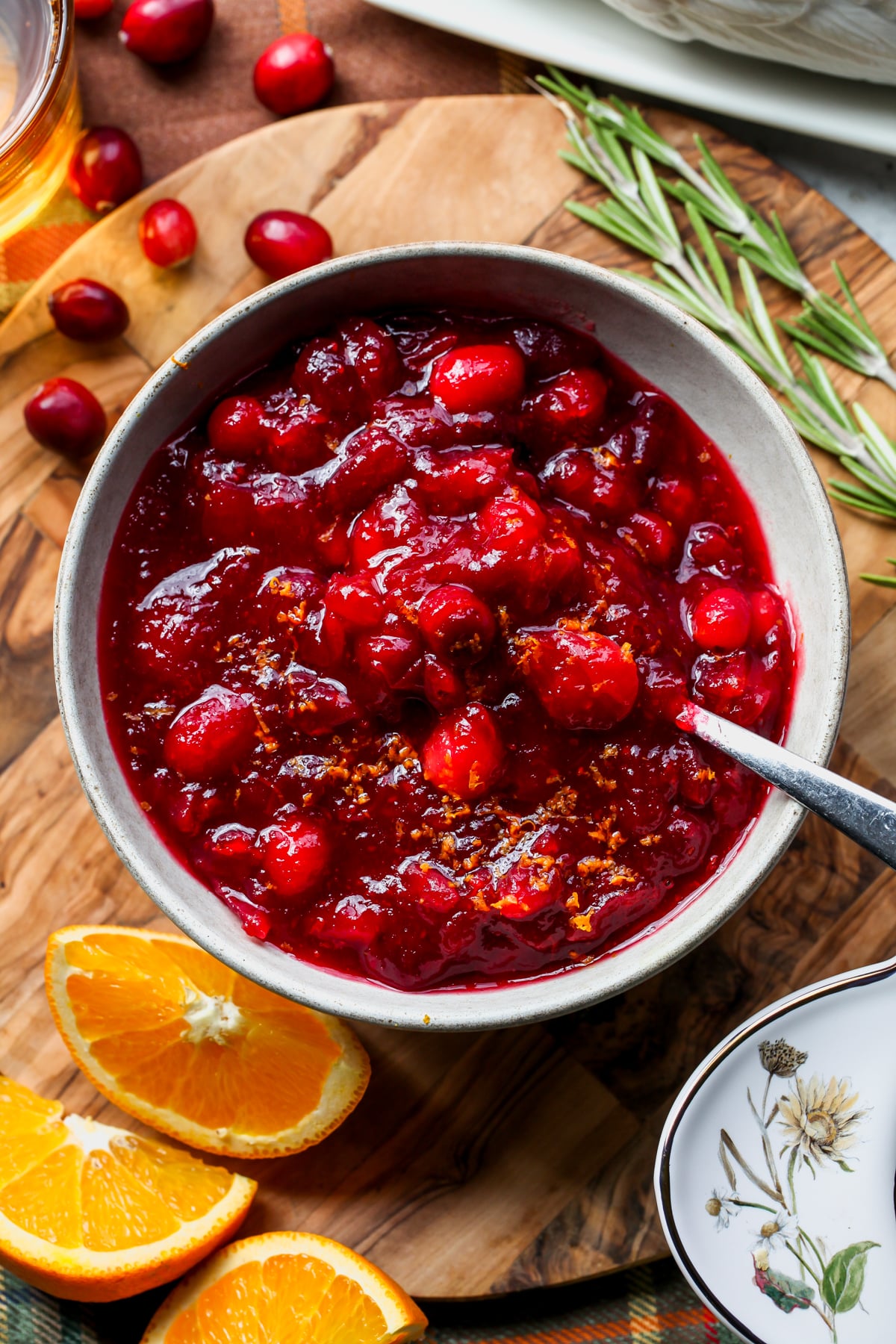 Homemade cranberry sauce on a round wooden board with a spoon resting on the right side.