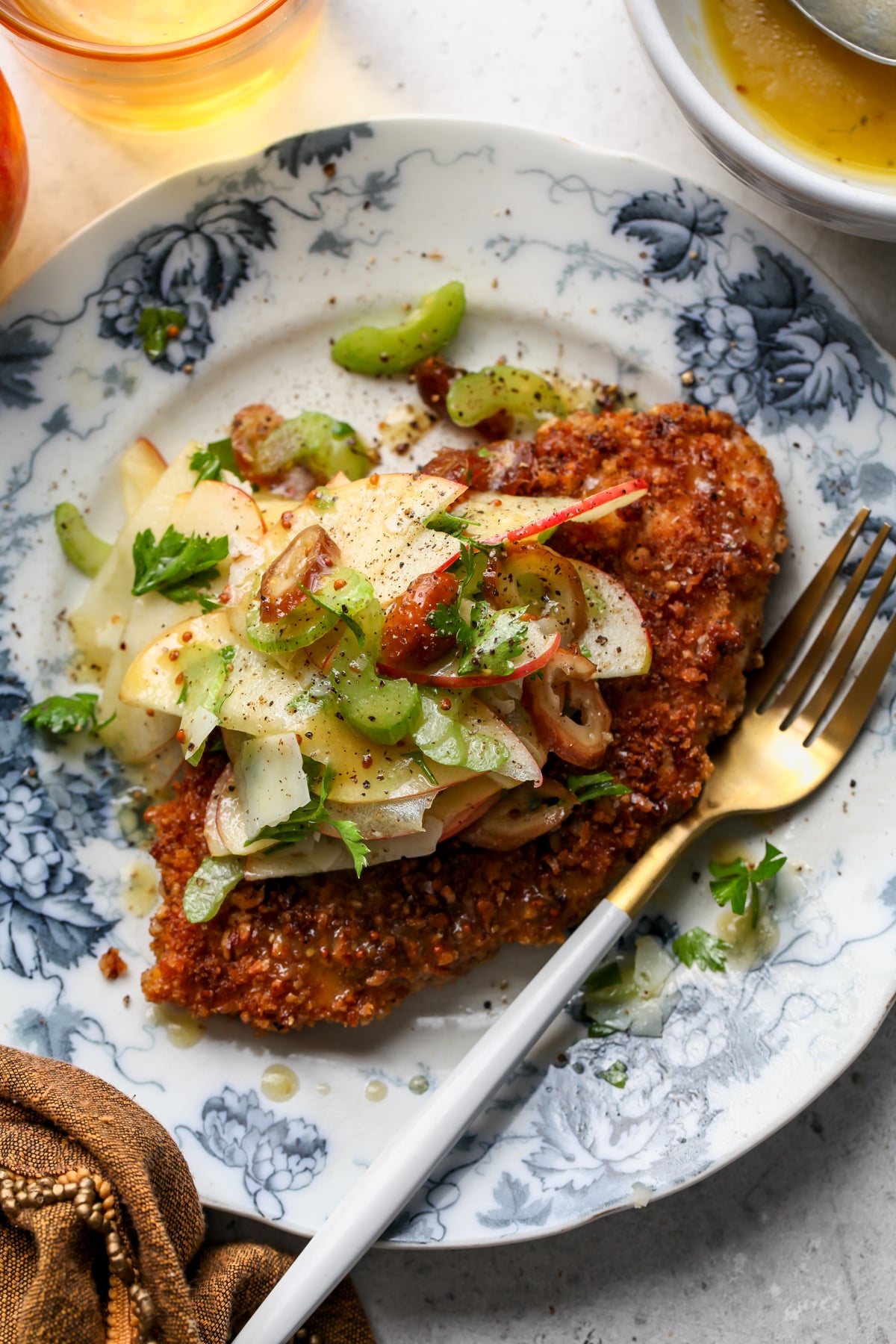 Pecan-crusted chicken cutlet on a white and blue plate topped with apple-celery salad.