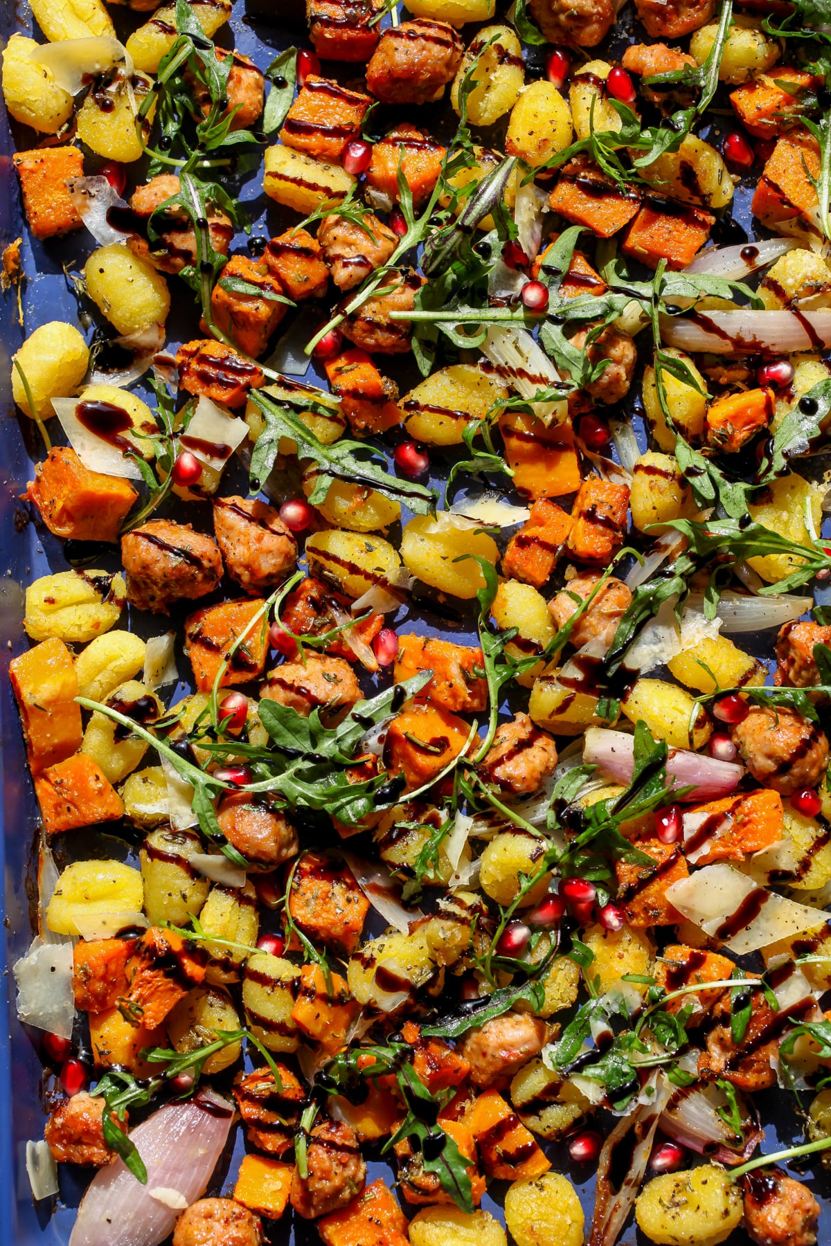 Sheet Pan Gnocchi with Chicken Sausage, squash, and shallots drizzled with balsamic glaze on a blue sheet pan.